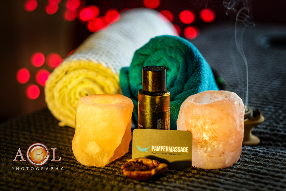 candles, massage oil and Pamper Massage business card on a massage bed